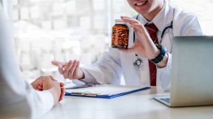 Young Male doctor giving pills bottle to female patient in clinic.