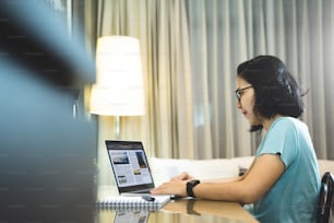 アジア人女性フリーランサーデザイナーは、夜間にラップトップコンピュータで作業する眼鏡をかけています。自宅で勉強し、オンライン学習をしている若い女子学生。ソーシャルディスタンス、ニューノーマルライフのコンセプト。