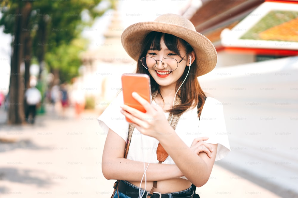 Hipster young asian energetic glasses girl modern style. Listen stream music with smart phone application. Summer backpack travel in city landmark. Happy solo outdoor style leisure. Bangkok, Thailand.