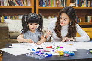 Asian girl kid and mother doing drawing with many color pencils on white paper