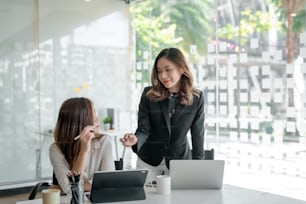 Two young beautiful asian business woman in the conversation, exchanging ideas at work.