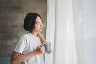 Morning Relaxation. Happy Asian man relaxing and enjoying coffee on holidays. Standing, Eyes closed, Breathing Fresh air.
