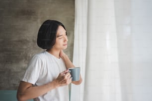 Relax mattutino. Uomo asiatico felice che si rilassa e si gode il caffè in vacanza. In piedi, con gli occhi chiusi, respirando aria fresca.