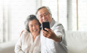 아시아 노부부는 스마트폰으로 셀카 사진을 찍으면서 즐거운 시간을 보내고 있다. 행복, 은퇴, 발렌타인 데이.