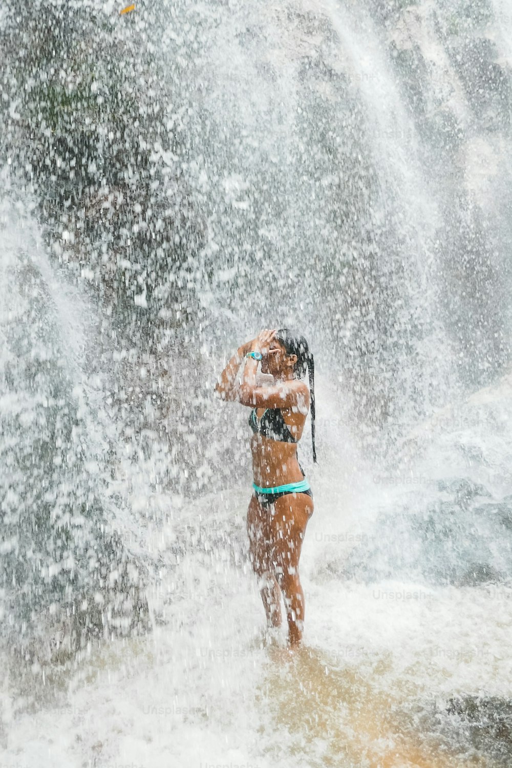 Woman under waterfall, on the bottom of rocks and river.