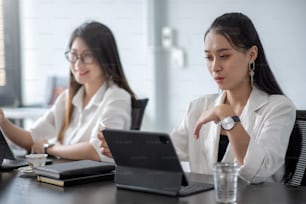 Due giovani donne d'affari asiatiche si scontrano con il pugno e utilizzano la tavoletta digitale con i loro colleghi in ufficio.