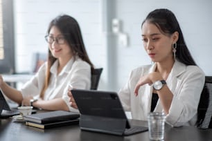 Deux jeunes femmes d’affaires asiatiques se cognent le poing et utilisent une tablette numérique avec leurs collègues au bureau.