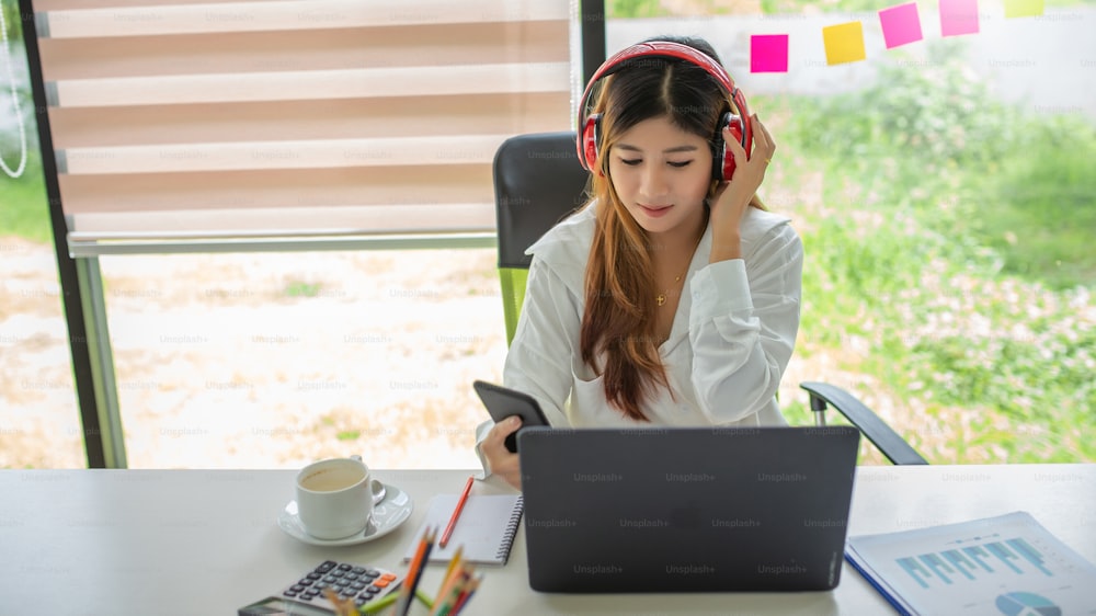 Mulher feliz. Mulher asiática jovem bonita que ouve música com fones de ouvido e usa o computador portátil.