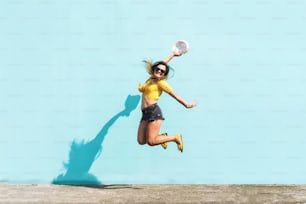 Porträt eines fröhlichen und niedlichen jungen hispanischen Mädchens, das vor Aufregung und Glück vor einer blauen Wand springt. Urbanes und fröhliches Konzept.