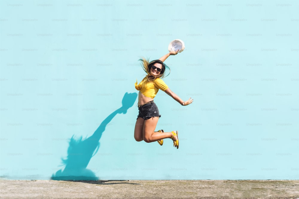 파란 벽 앞에서 흥분과 행복으로 점프하는 쾌활하고 귀여운 히스패닉 소녀의 초상화. 도시적이고 행복한 개념.