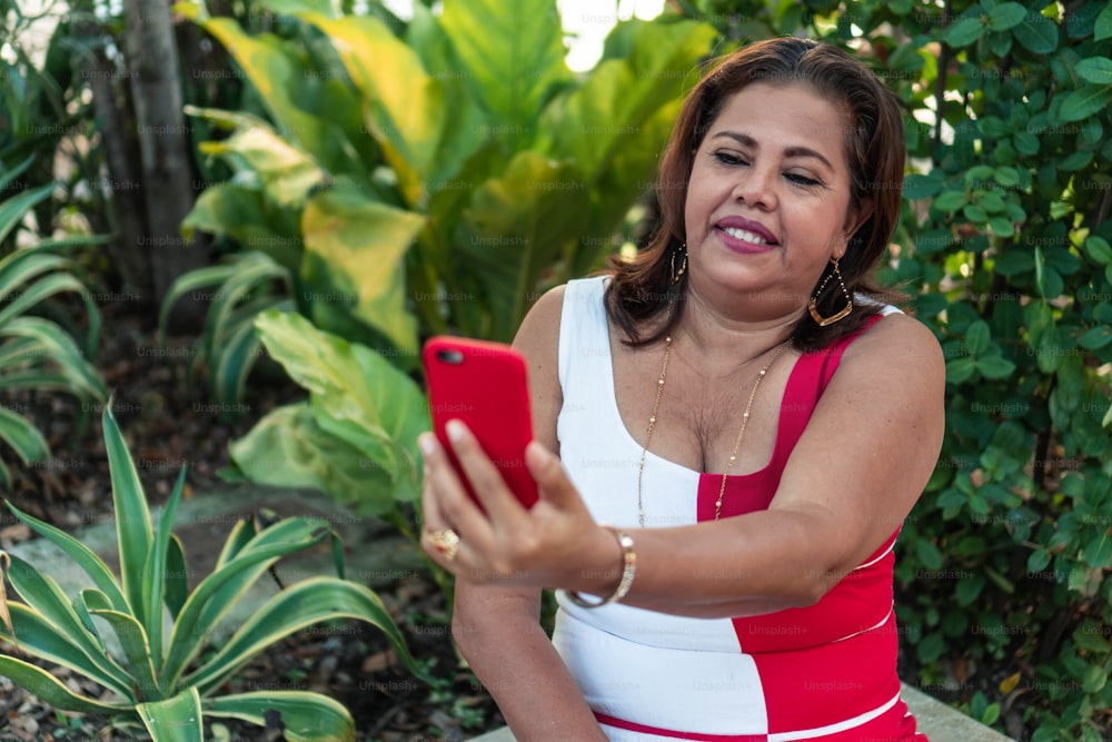 Attractive smiling older woman taking a photo on her smartphone as she sits alone in a public park