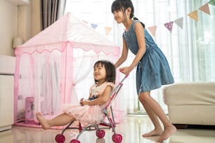 Asian little young girl daughter sibling feel happy and enjoy playing together in living room at home. Two sweet kid sister have fun on holiday vacation indoor at house. Activity relationship concept