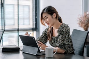 Bella giovane donna asiatica che lavora alla scrivania con tablet digitale in un ufficio moderno.