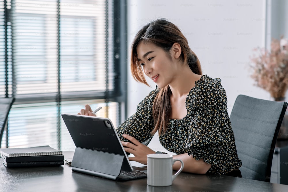 Pretty young asian woman working at desk with digital tablet in a modern office.