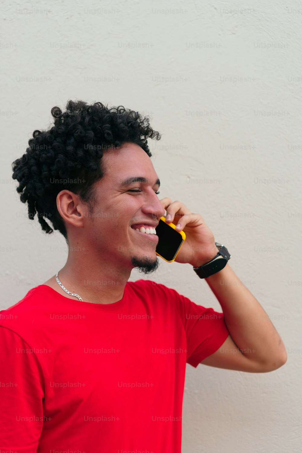 Retrato de um jovem rindo falando em um smartphone na frente de uma parede cinza.