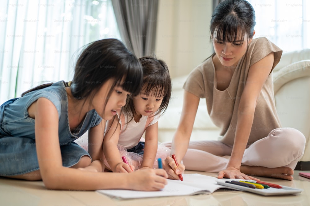 Asian loving parent spend time with small cute kid daughter enjoy activity at house. Little siblings girl artist having fun draw and color picture with mother on floor. Parenting relationship concept.