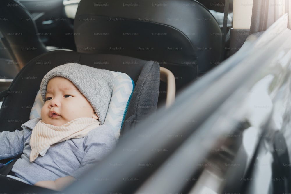 Portrait of Cute Asian newborn baby boy sitting on his car safety seat in the car while traveling.