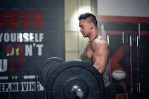 Strong young athlete fit man lifting the barbell weight in fitness gym. The man with sportswear showing his strength muscular in body. Bodybuilding exercise and sport workout training concept.