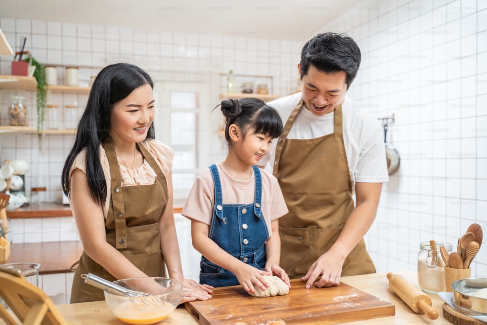 アジアの幸せな家族は、家にいて、キッチンで一緒に時間を過ごし、ベーカリーや食べ物を焼いています。幼稚園児は両親から学び、お父さんとお母さんは家で子育て活動の関係を楽しんでいます。