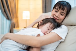 Asian beautiful loving mother hugging sleeping baby girl in her arms with gently. Parent holding small baby to rest on shoulder and sleep with young daughter. Parenting relationship at home concept.