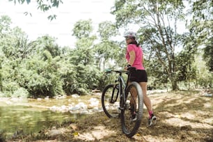 horizontal photograph of a hispanic latin american woman in sportswear for cycling holding a walking bicycle. nature and outdoors concept.