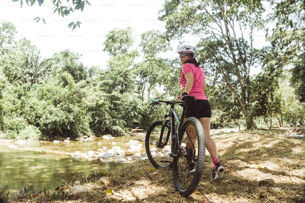 horizontal photograph of a hispanic latin american woman in sportswear for cycling holding a walking bicycle. nature and outdoors concept.