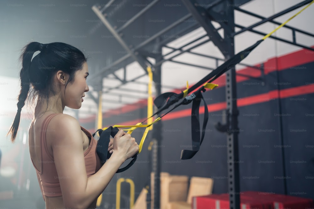 Ragazza atleta attiva asiatica dritta le braccia per tenere la corda ancorata a una trave d'acciaio nello stadio. Sollevamento su e giù per mantenere i muscoli, costruire forza, flessibilità in palestra o in palestra