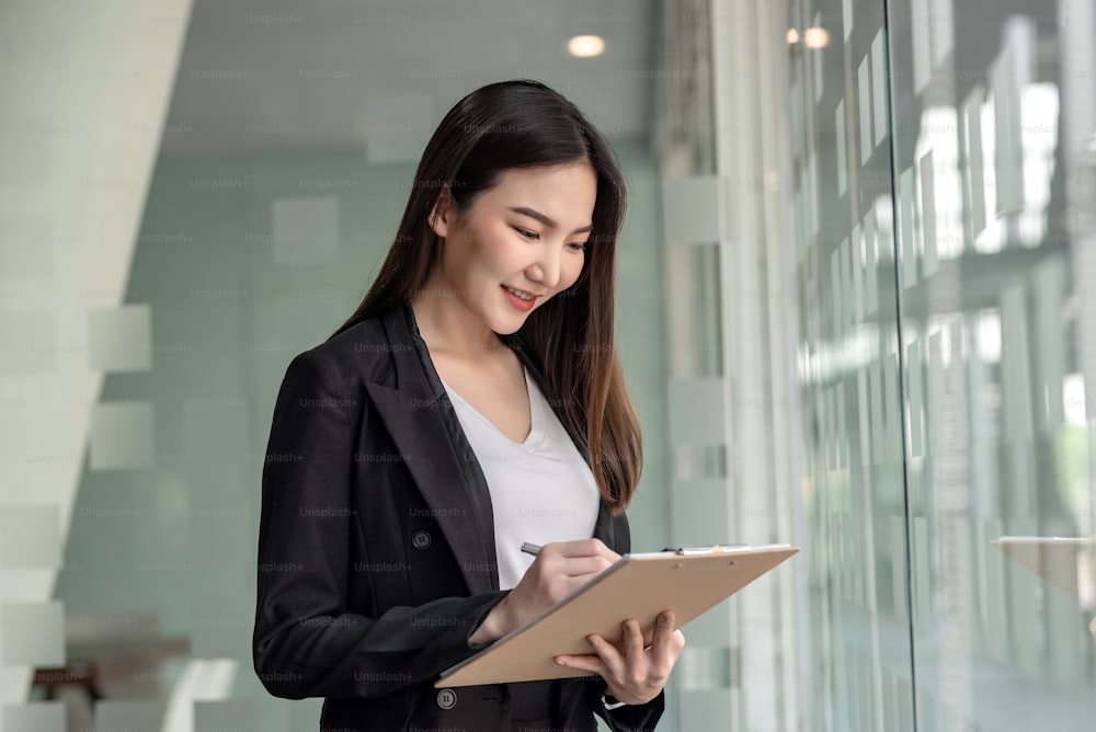 Asian business woman holding a document standing near a mirror at an office.