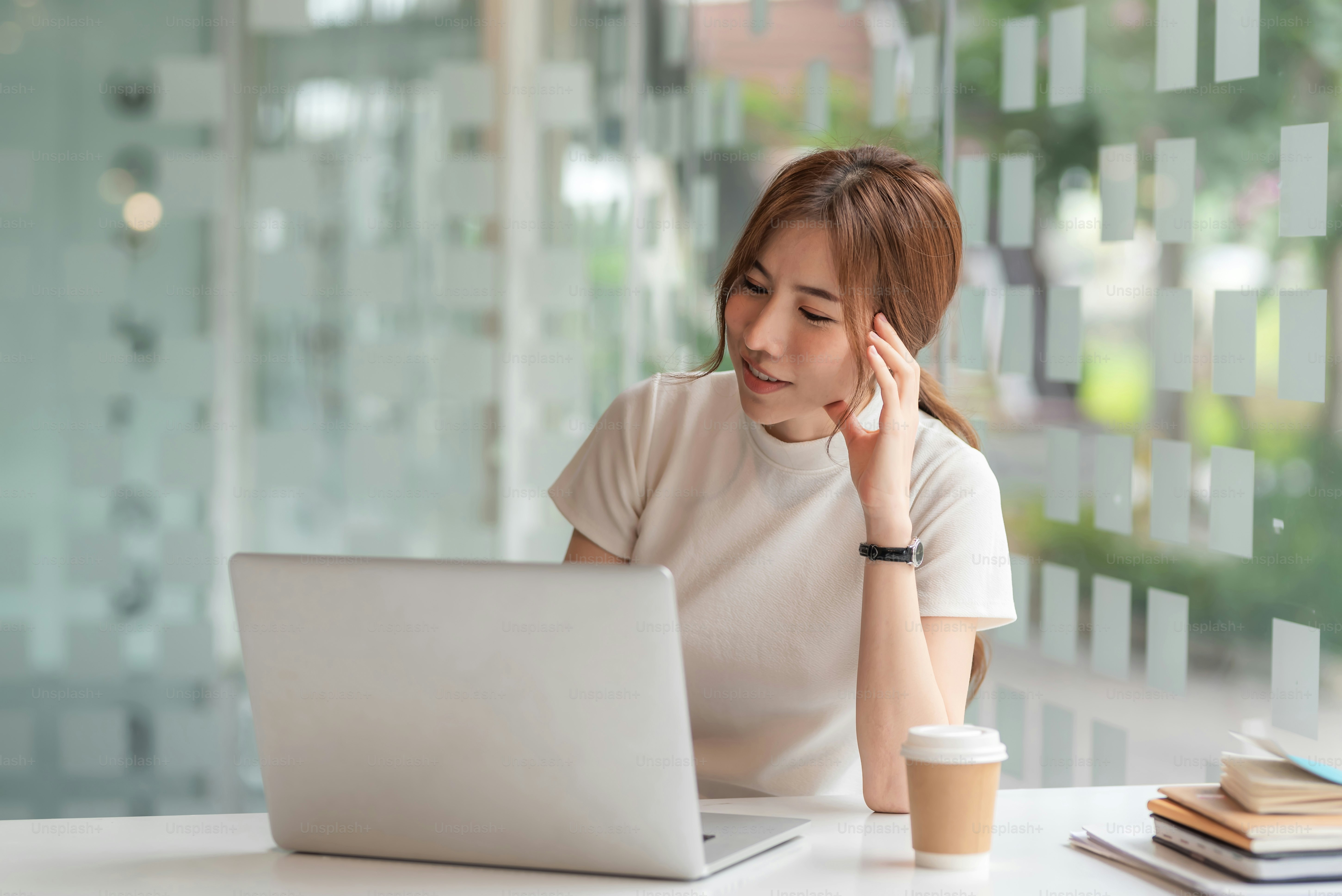 La donna asiatica felice si è seduta guardando la tazza di caffè del laptop posta al tavolo del bar.