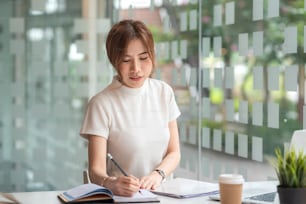 Vista frontal de una hermosa mujer asiática tomando notas en el trabajo de oficina.