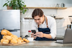 Asian businessman cafe owner take photo of cup of coffee for marketing. Young barista man restaurant worker use laptop computer enjoy post advertising picture for online digital social network content