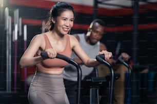 Athlete sportsman and woman exercising bike exercise machine in stadium. Group of multiethnic fitness trainer cardio workout, use stationary bicycle for bodybuilding and strengthen muscle in fitness gym