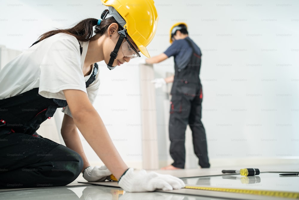 Asian Craftsman or Carpenter worker man and woman wear safety helmet and eyeglasses, work by lays parquet on corridor. Joiner Builder installs laminate board on floor to renovating apartment or house.