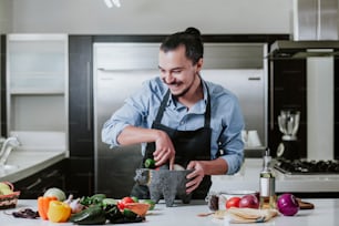 メキシコシティの自宅のキッチンでサラダやメキシカンソースを準備するラテンの男性が自宅で料理をしています