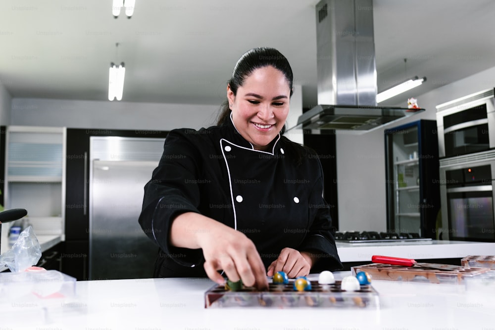 mulher latina chef confeiteiro vestindo uniforme preto no processo de preparação de deliciosos chocolates doces na cozinha no México América Latina