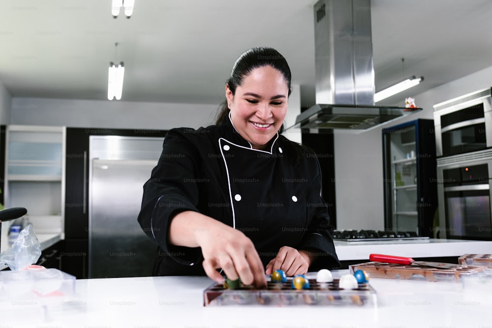 pasticcere latino donna che indossa uniforme nera in corso di preparazione di deliziosi dolci cioccolatini in cucina in Messico America Latina