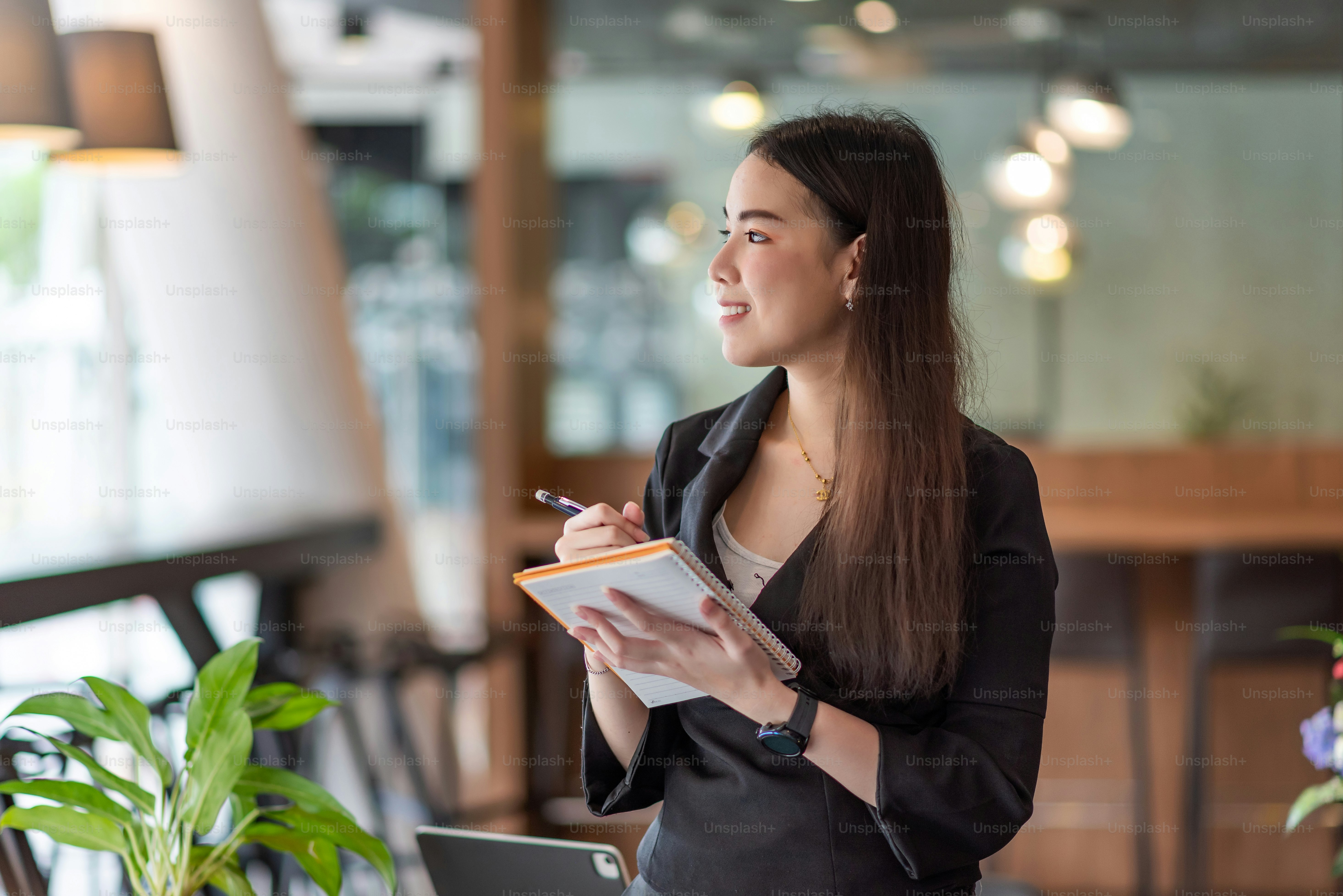 Side view of an Asian businesswoman sitting at the office looking out the window holding a pen and notebook. working concept.