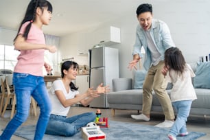 Asian family spending time together on holiday in living room at home. Attractive happy parents, father play with young little two kid girl daughter run around mother at home. Activity relationship.