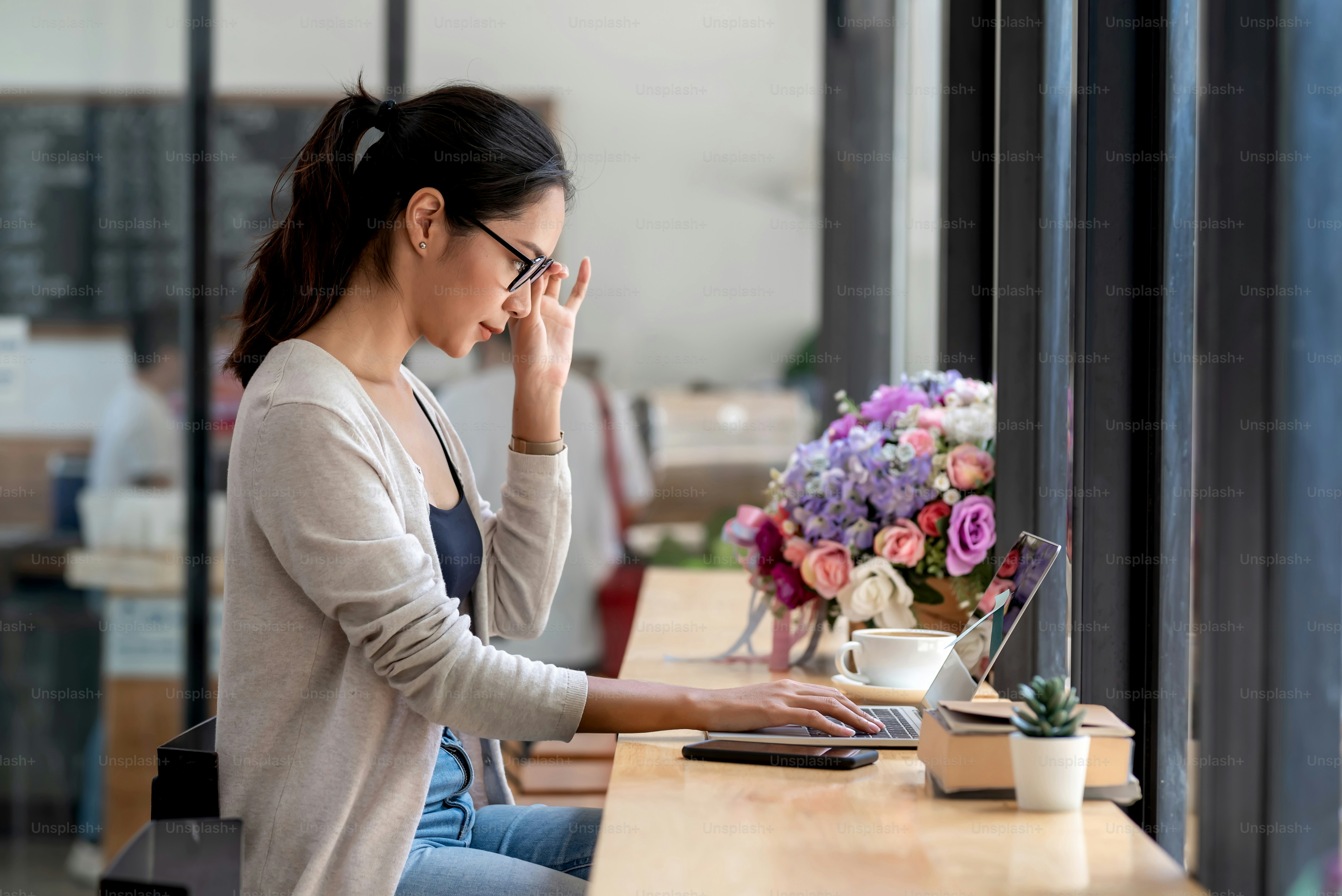 Side view of young Asian businesswoman wearing glasses to work using a tablet smartphone placed on the office desk.