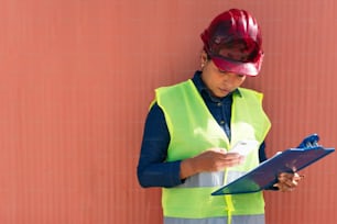 Hispanic woman with protective vest checking her cell phone in a factory