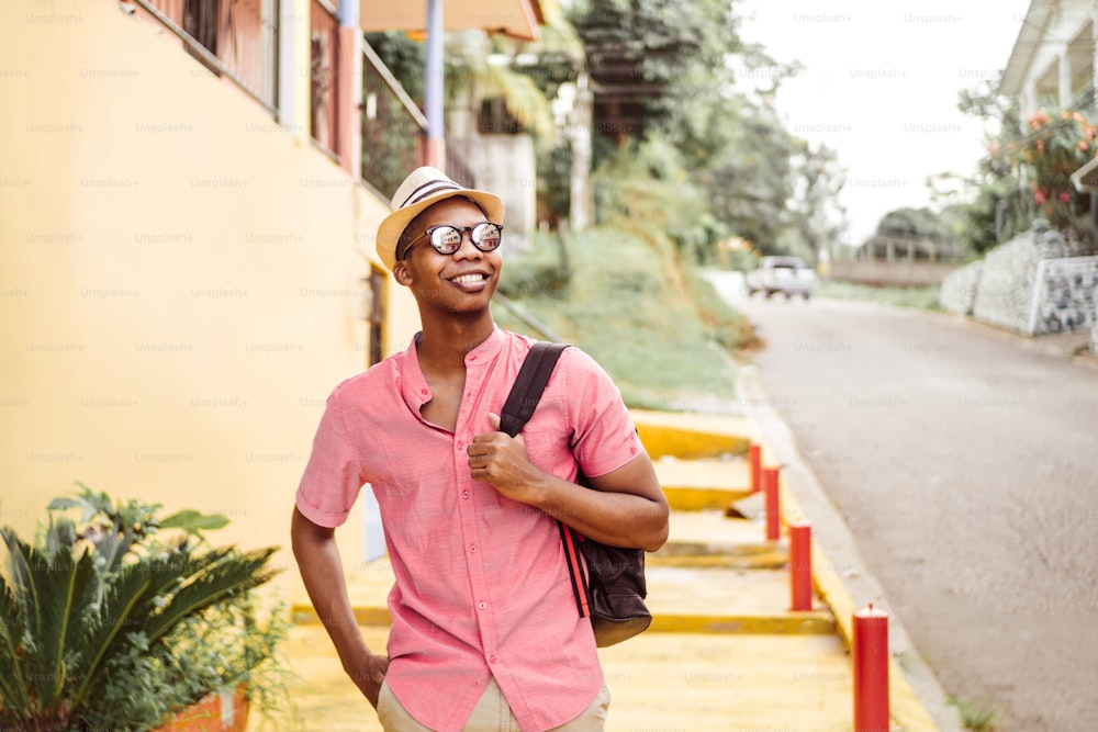black young adult tourist go with eyeglasses holding a backpack walking on latin american neighborhood.