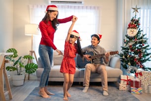 Asiatische nette Familienmitglieder genießen es, Weihnachtslieder zusammen zu Hause zu singen. Junge kleine Tochter, die sich glücklich und aufgeregt fühlt, um die Weihnachtsfeier zusammen mit den Eltern im Haus zu feiern.