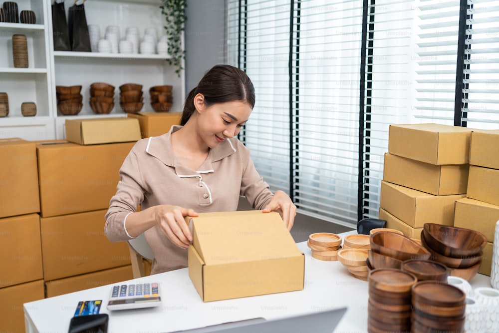 Asiatische schöne Frau verpackt Vase Waren bestellen in Box für Kunde. Junges attraktives Geschäftsmädchen, das an der Vorbereitung von Paketkästen arbeitet, die den E-Commerce-Versand im Online-Handel überprüfen, um ihn zu Hause zu verkaufen.