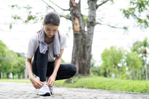公園を走る前に靴ひもを結ぶアジアの美しいスポーツ女性。庭の通りで夕方の夕暮れ時に彼女の健康的な健康のために屋外でジョギングトレーニングを行うことで、スポーツウェアの運動で魅力的なアスリート