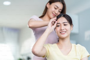 Asian beautiful lesbian women couple combing girlfriends hair in house. Attractive two female gay friend sit on sofa in living room, feel happy for beauty cosmetic together. Homosexual-LGBTQ concept.