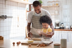 Playful African American boy enjoy cooking with his father in kitchen together. Black Family doing bakery at home.