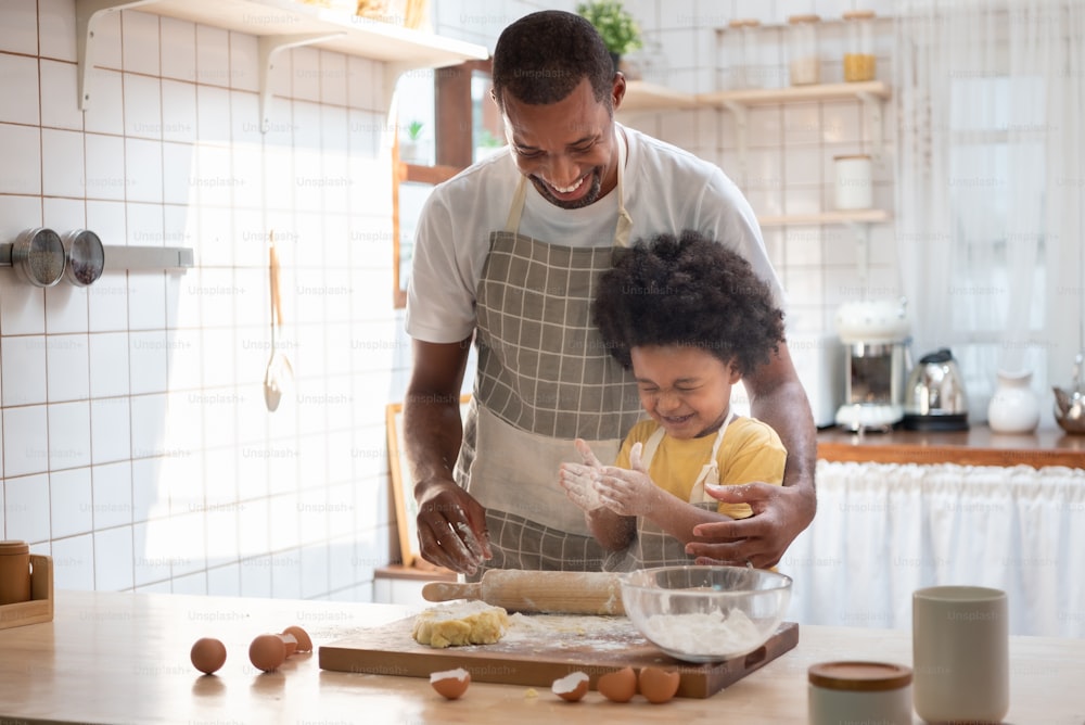 Il ragazzo afroamericano giocoso si diverte a cucinare con suo padre in cucina insieme. Famiglia nera che fa la panetteria a casa.