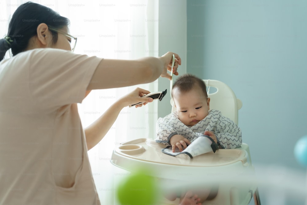 Asian Cute little baby boy getting his hair cut by his mother at home.