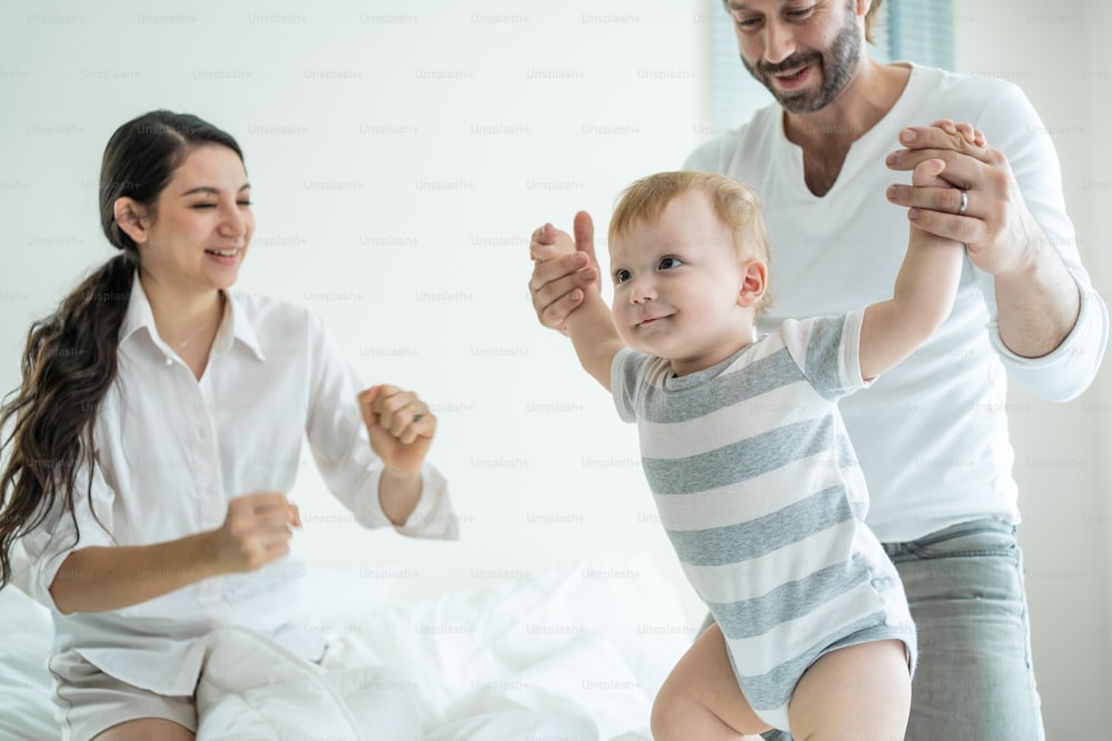 백인 사랑하는 부모는 침실의 침대에서 아기 아이와 놀고 있습니다. 행복한 가족, 매력적인 아름다운 젊은 커플 아빠와 엄마는 귀여운 유아 유아 아들과 함께 춤을 추며 기상 후 아침 활동을 즐깁니다.