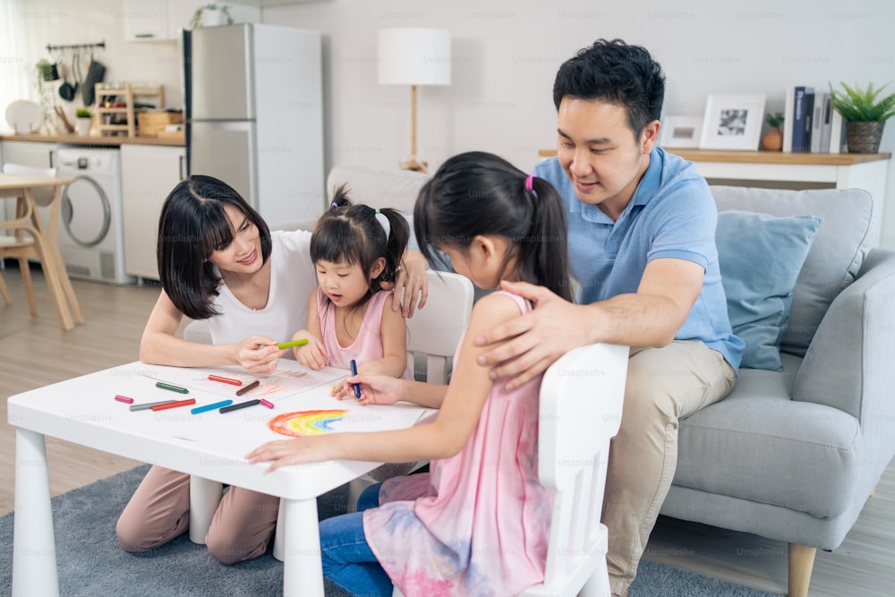 Asian young kid daughter coloring and painting on paper with parents. Happy family activity, Little girl children learn how to draw art picture enjoy creativity with mother and father in living room.